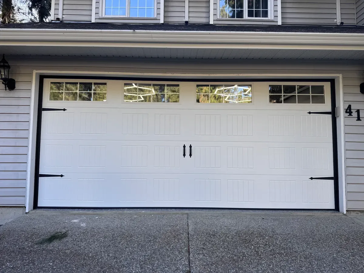 A white carriage-style garage door with black strap hinges and glazed top panels on a beige two-storey home