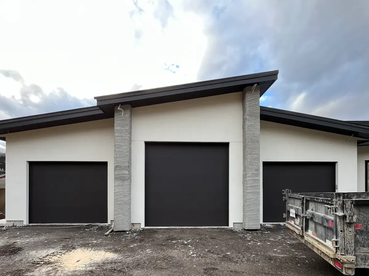 Three black flush-panel garage doors on a white stucco modern home