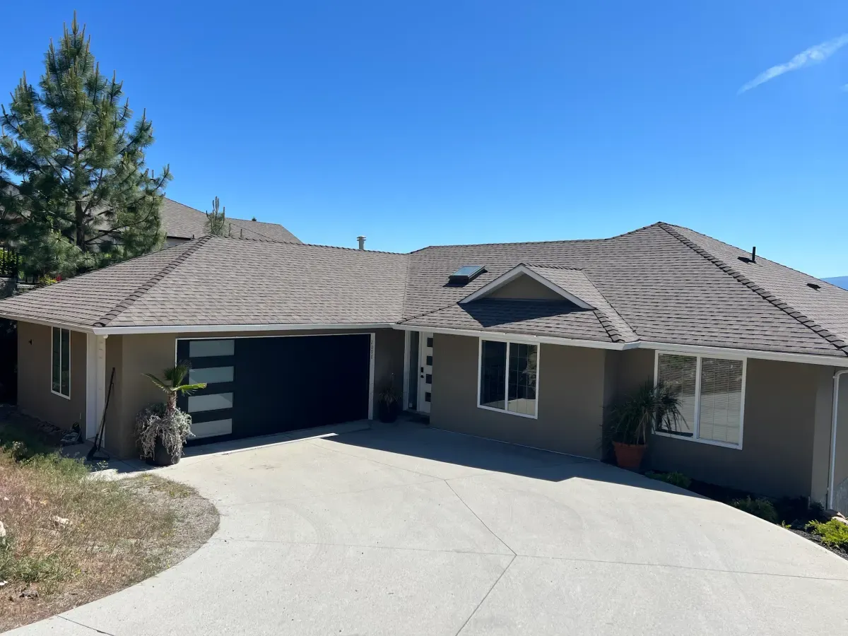 A dark modern garage door on a tan Okanagan bungalow with a concrete driveway