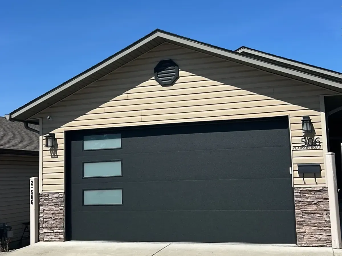 A black modern garage door with three frosted vertical windows on a tan home with stone accents