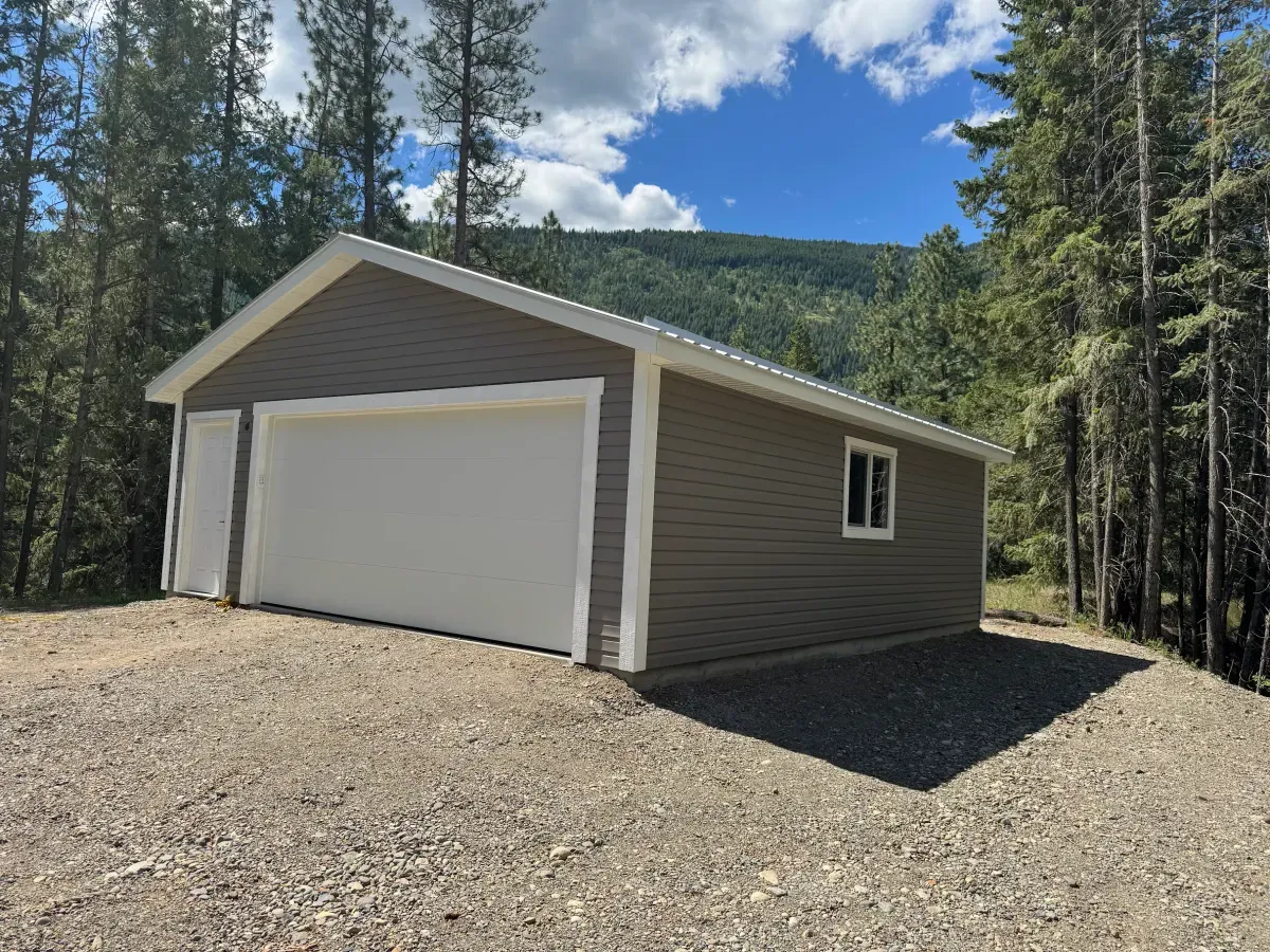 A white garage door on a new detached garage against the Monashee forest