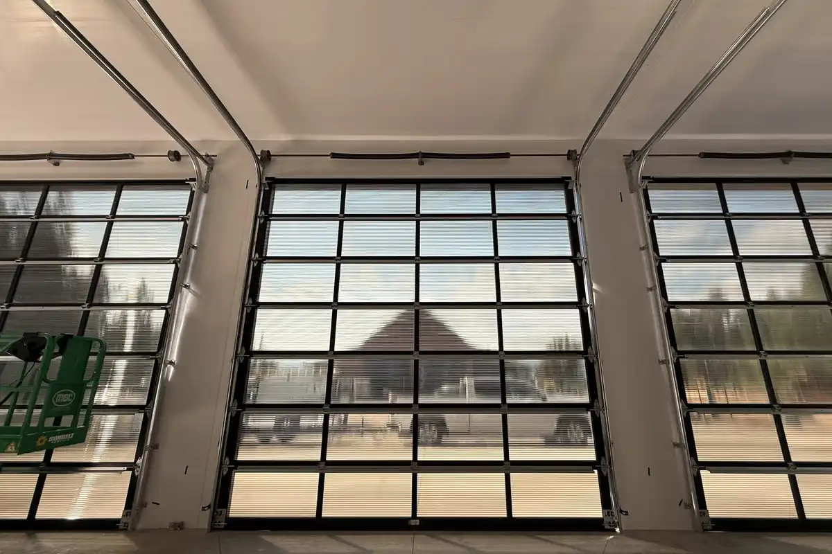 Three black-framed full-view garage doors installed along the wall of a new shop, seen from inside